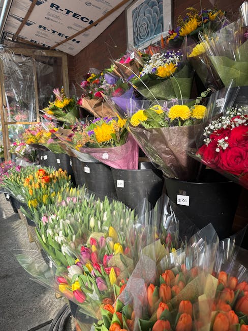 A variety of freshly cut flower bouquets displayed on black bins inside a flower shop, featuring a mix of vibrant blooms such as yellow chrysanthemums, purple irises, red roses, pink and orange tulips