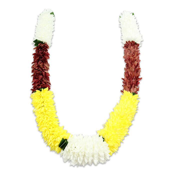 A richly coloured U-shaped garland rests against a pristine white field, photographed to show its sculptural curve and the subtle shadow that gives it dimension. At the top of each arm a dense cylinder of snowy white, small-petalled flowers-suggestive of tiny chrysanthemums or densely packed jasmine reproductions-creates a soft, auspicious cap. Below each white cuff, a compact, maroon or dark terracotta-red band adds a concentrated, grounding tone; its tiny fabric petals are arranged in tight clusters that read as tactile and warm. The longest portion of the garland sweeps into a broad field of cheerful yellow blooms, their plush texture and crowded placement forming the graceful lower curve of the U. Where the two yellow sections meet at the bottom, a generous rosette of pure white chrysanthemum-like flowers becomes the central focal point, framed by small, dark-green leaf-like accents that mark the colour transitions and lend a hint of natural contrast. The materials are artificial fabric and thread-meticulously layered to emulate natural blossoms-so the garland is durable for repeated ceremonial use. Light plays gently across the petals, revealing the care in handwork and the evenness of the assembly. Visually and culturally, the white, yellow and maroon palette signals purity, prosperity and devotion; this style of mala is suited to Hindu puja, temple offerings, weddings, and festivals such as Diwali or Holi, and will sit comfortably in both a family altar on a quiet Canning Town terrace and a formal offering at a community celebration near the Royal Docks.