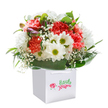 A lively bouquet, brimming with fresh, uplifting spirit, sits gracefully within a modern white gift bag-its simplicity drawing focus to the vibrant display within. The ruffled coral and peach carnations radiate warmth, each petal layered and gently curled with delicate precision. Nestled beside them, bright white daisies with golden-green eyes beam with gentle optimism, their crisp petals offering an irresistible contrast. Wispy, ethereal sprays of white baby's breath wind through the composition, adding airy brightness reminiscent of peaceful mornings by Canning Town Recreation Ground. Subtle hints of purple-tinged buds peek out among the florals, promising the excitement of new beginnings and the delight of the unexpected. Encasing the arrangement, glossy dark green leaves provide a lush, natural foundation, enhancing the vibrancy of every blossom and granting structure to the display. The balanced, rounded form of the bouquet speaks to the thoughtful design of local florists-each stem selected with care, each detail purposeful. Resting in a crisp, square white gift bag with robust ribbon handles, the bouquet is perfectly suited for celebratory occasions, heartfelt gestures, or simply bringing cheer to everyday life in E16, whether delivered to a neighbour on Barking Road or a friend near the Excel Centre. It's a joyful tribute to the artistry and freshness of Canning Town's floral scene, designed to lift spirits and share beauty in every community moment.