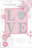 This anniversary card presents a gentle celebration of lasting romance, its design as soft and reassuring as an evening walk through the quieter streets of Canning Town. The central focus is the word LOVE, rendered in raised, velvety glitter that adds a three-dimensional feel to the card. Each letter is pale and luminous, with the O replaced by a shimmering silver heart, lightly textured so it seems to glow against the blush-pink backdrop. Around this heartfelt centrepiece, delicate blossoms and trailing vines unfurl in tones of blush, mauve, ivory, and gentle grey. The floral illustrations have an almost watercolour softness, with fine, flowing outlines that give them the look of petals and foliage sketched by a florist planning a romantic arrangement for delivery near Custom House or along Hermit Road. Small flourishes-tiny petals, curling swirls, and subtle butterfly shapes-dance in the spaces between, suggesting motion and adding a touch of whimsy, like a light spring breeze through an English cottage garden. The overall colour palette blends pastel pinks and silvery greys, creating an atmosphere of treasured intimacy rather than bold celebration. Elegant, understated script spells out tender phrases such as On Our Anniversary and I love you today and always, the lettering gently echoing the curves of the vines. Soft lighting across the card's surface accentuates the mix of smooth paper, raised glitter, and faint metallic highlights. The composition feels like a keepsake to be cherished, capturing not just the occasion, but the quiet, ongoing story of two people who choose each other, day after day, in their shared Canning Town home.
